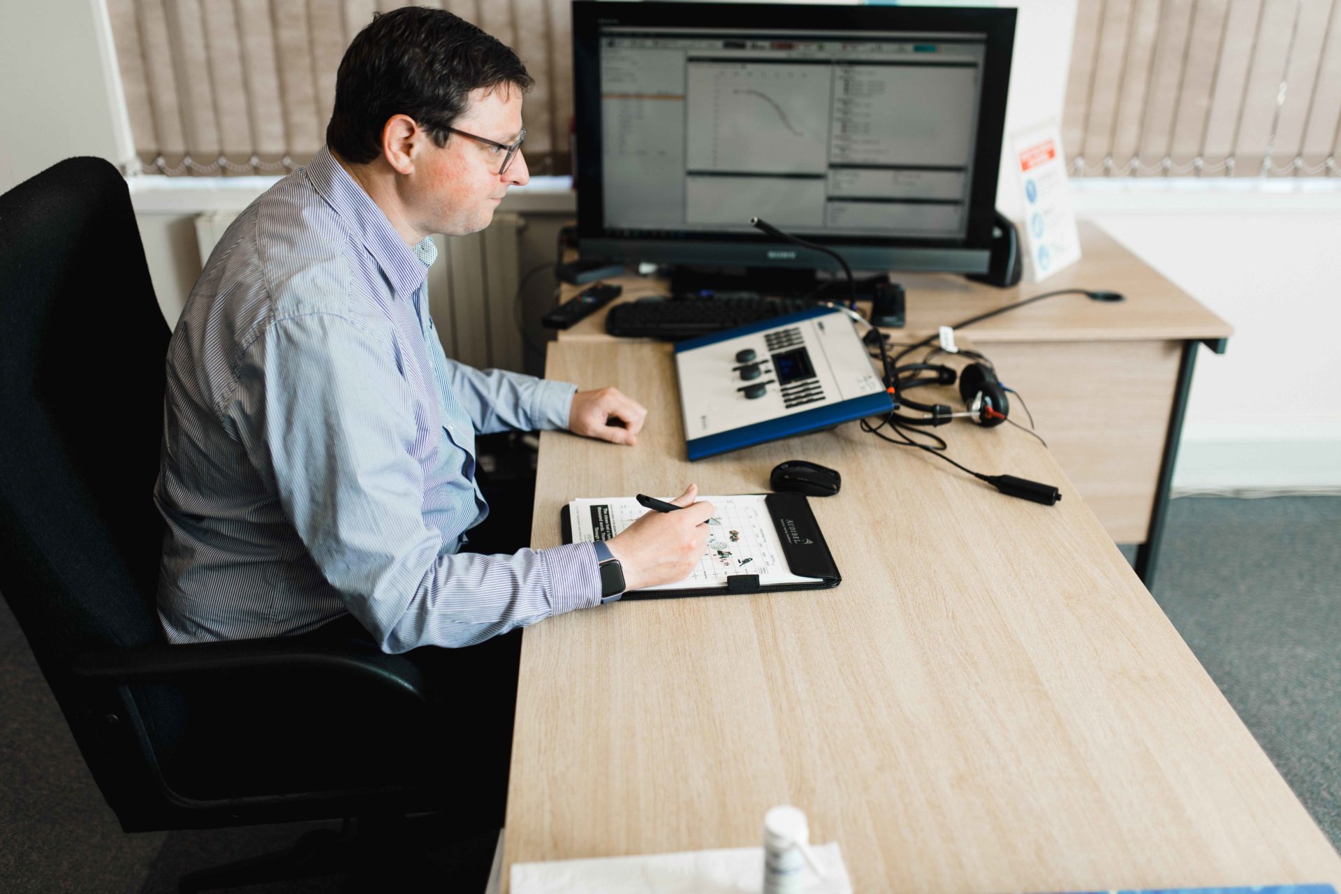 professional audiologist conducting hearing test and filling in results