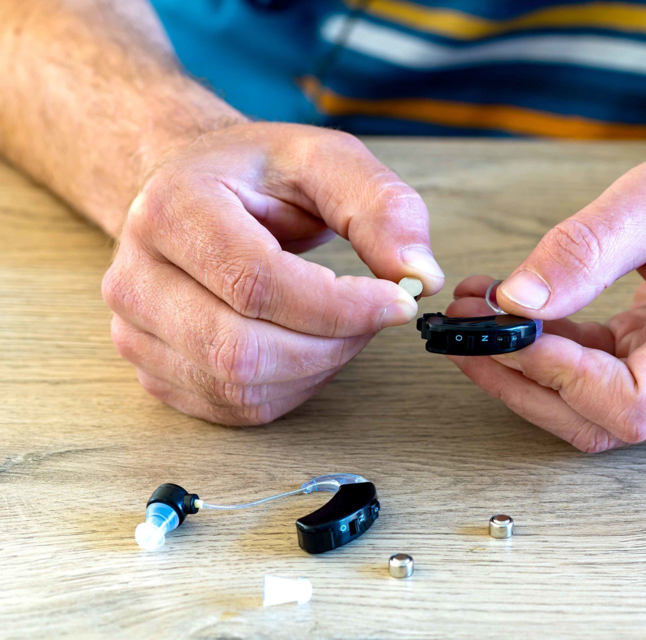 man fitting new set of hearing aid batteries in hearing aid