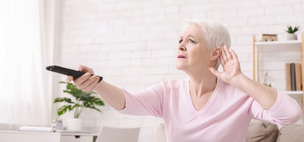 a woman turning up the volume of the tv as she struggles to hear it.