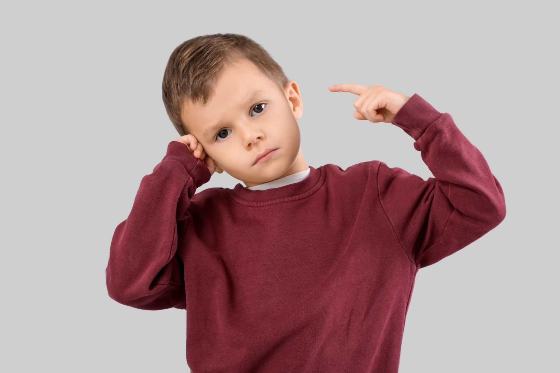 Boy pointing to his right ear whilst holding the left