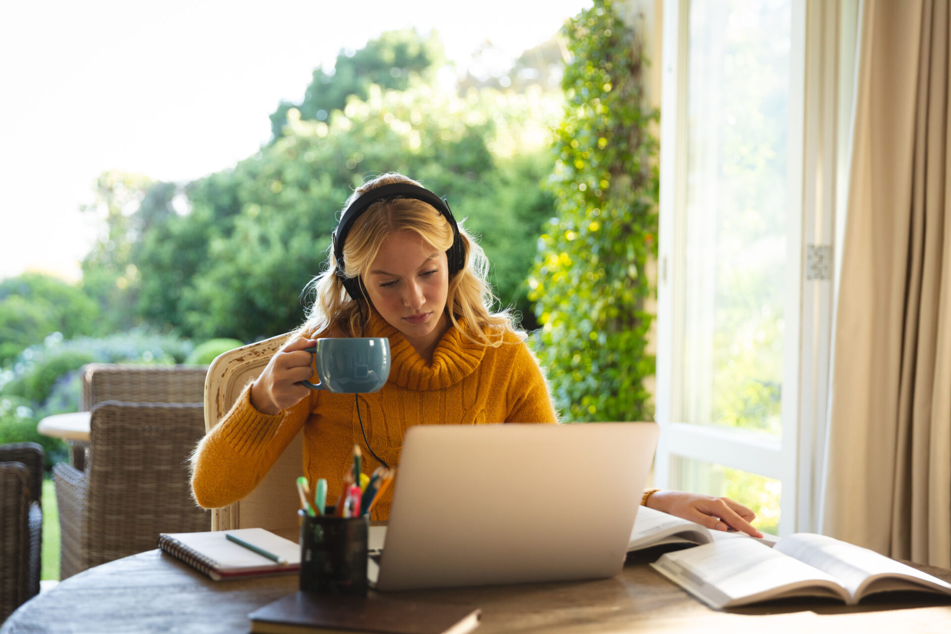 woman working in living room at home, wearing headphones and using laptop